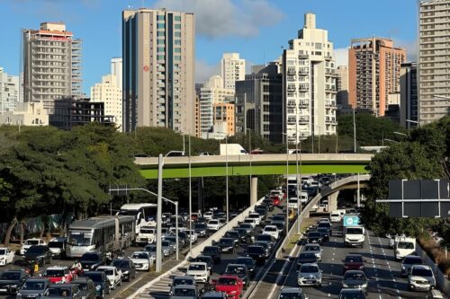 Trânsito intenso em avenida de São Paulo durante o feriado estadual de 9 de julho, com carros e prédios ao fundo.