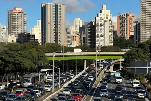 Trânsito intenso em avenida de São Paulo durante o feriado estadual de 9 de julho, com carros e prédios ao fundo.