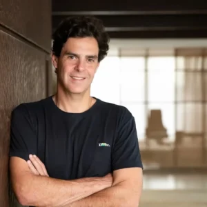 Guilherme Benchimol posa de braços cruzados durante a Expert XP 2026, representando imagem sobre os 25 anos da companhia.