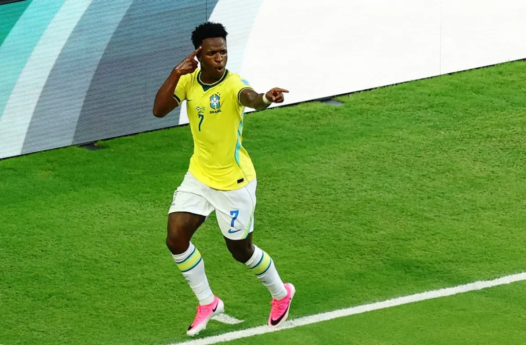 Vinícius Júnior comemora gol durante partida em campo de futebol, representando o jogador mais rico da Seleção Brasileira na Copa 2026.