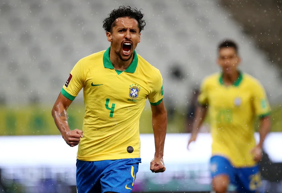 Marquinhos comemora gol pela Seleção Brasileira durante partida, com expressão vibrante e uniforme amarelo.