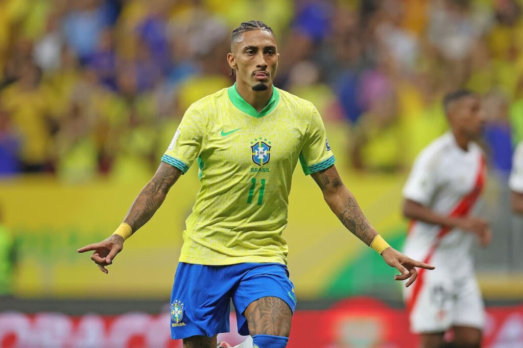 Raphinha com a camisa da Seleção Brasileira durante partida, em ação no gramado de estádio de futebol.