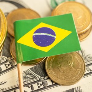 Bandeira do Brasil sobre moedas e notas de dólar, representando economia, inflação e investimentos.