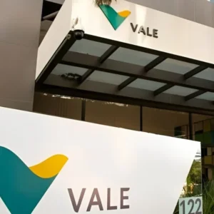 Placa com o logotipo verde e amarelo da Vale em primeiro plano e fachada de prédio corporativo ao fundo.