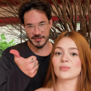 Uma foto em plano fechado da influenciadora digital Viih Tube e de seu parceiro Eliezer. À direita, Viih Tube aparece em primeiro plano, encarando a câmera com uma expressão séria; ela tem longos cabelos ruivos e lisos, pele clara e um pequeno piercing no nariz. Logo atrás dela e ligeiramente à esquerda, Eliezer olha para a câmera com um leve sorriso.
