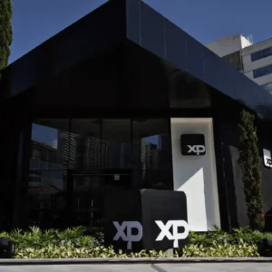 Fachada da sede da XP Investimentos com logotipos da empresa em área externa cercada por jardins e edifícios.