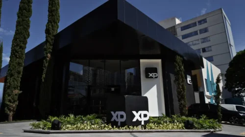 Fachada da sede da XP Investimentos com logotipos da empresa em área externa cercada por jardins e edifícios.